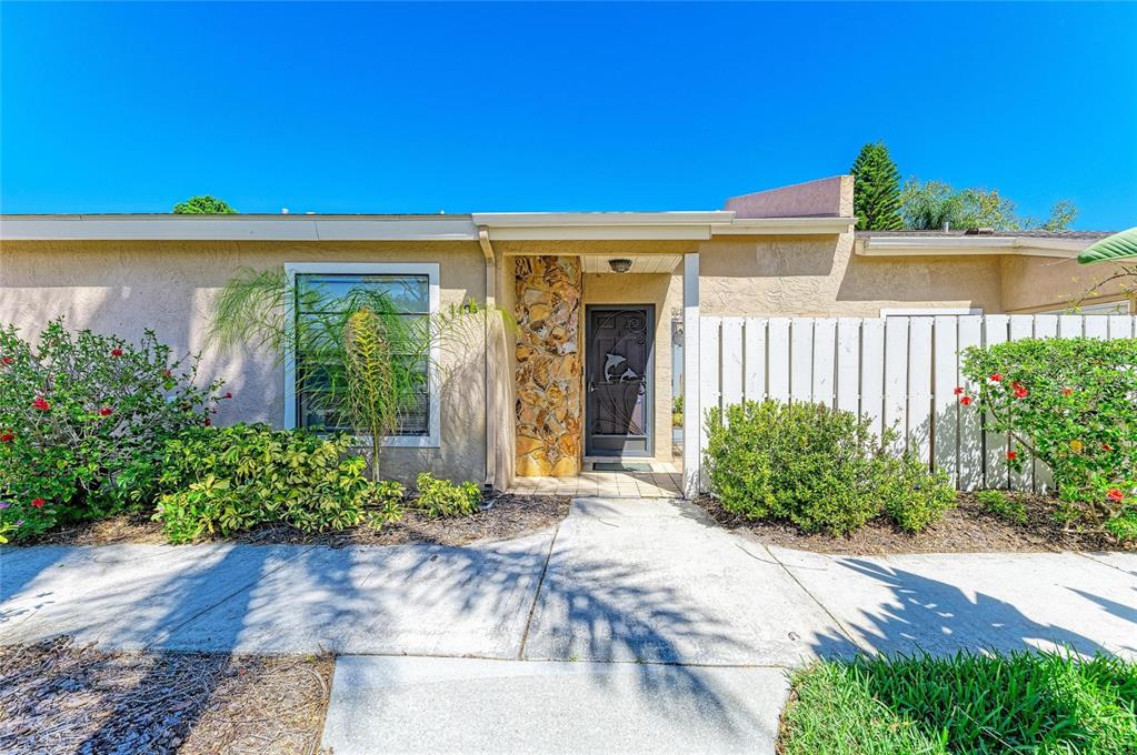 A single-story house exterior features a stone-accented entryway, a dark front door, and landscaping — 3405 TALLYWOOD LANE UNIT 7130, SARASOTA, FL