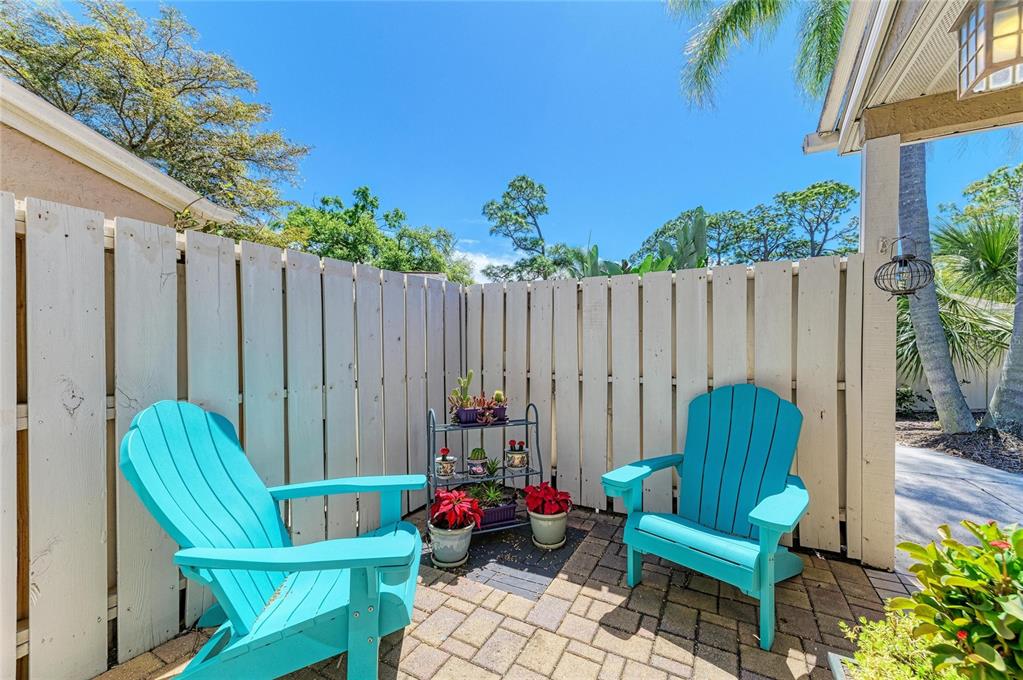 A small brick patio features two bright blue Adirondack chairs and a metal plant stand — 3405 TALLYWOOD LANE UNIT 7130, SARASOTA, FL