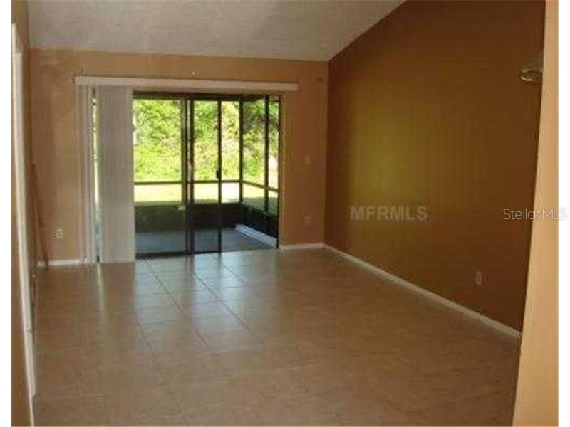 An empty living room features light-colored tile flooring, a vaulted ceiling, and sliding glass doors — 104 CREEKSIDE WAY, ORLANDO, FL