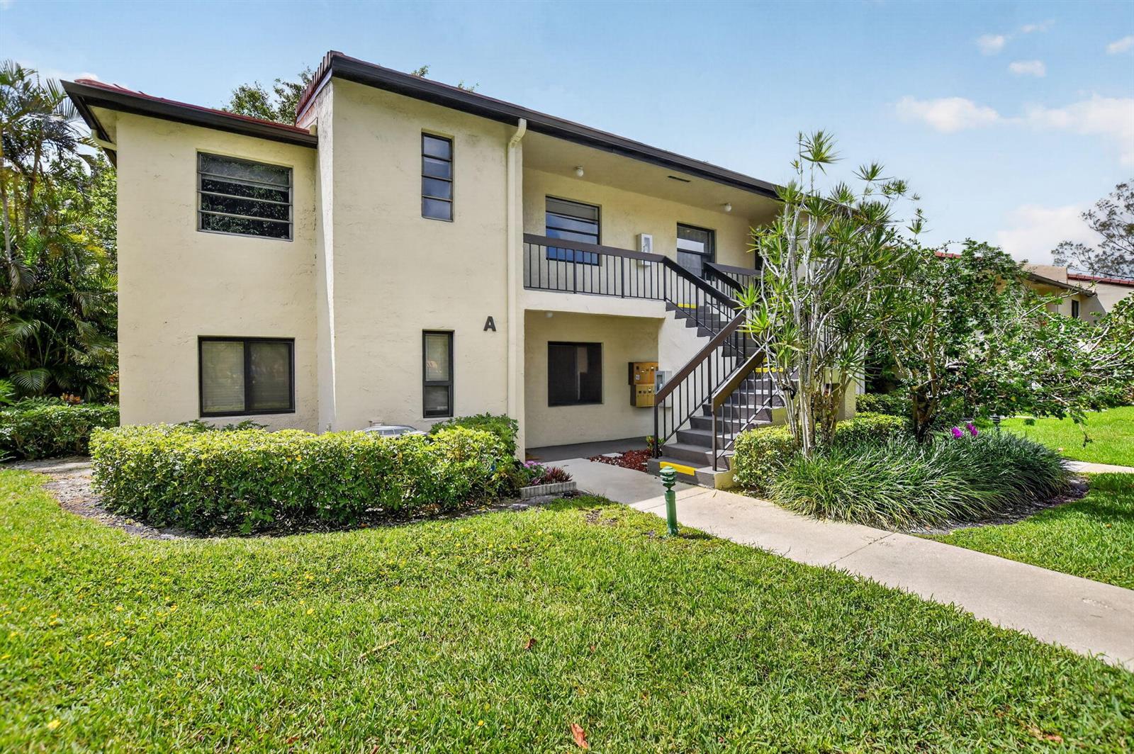 A two-story apartment building with a beige exterior, a staircase, and a landscaped lawn — 8310 Casa Del Lago # D, Boca Raton FL 33433, BOCA RATON, FL