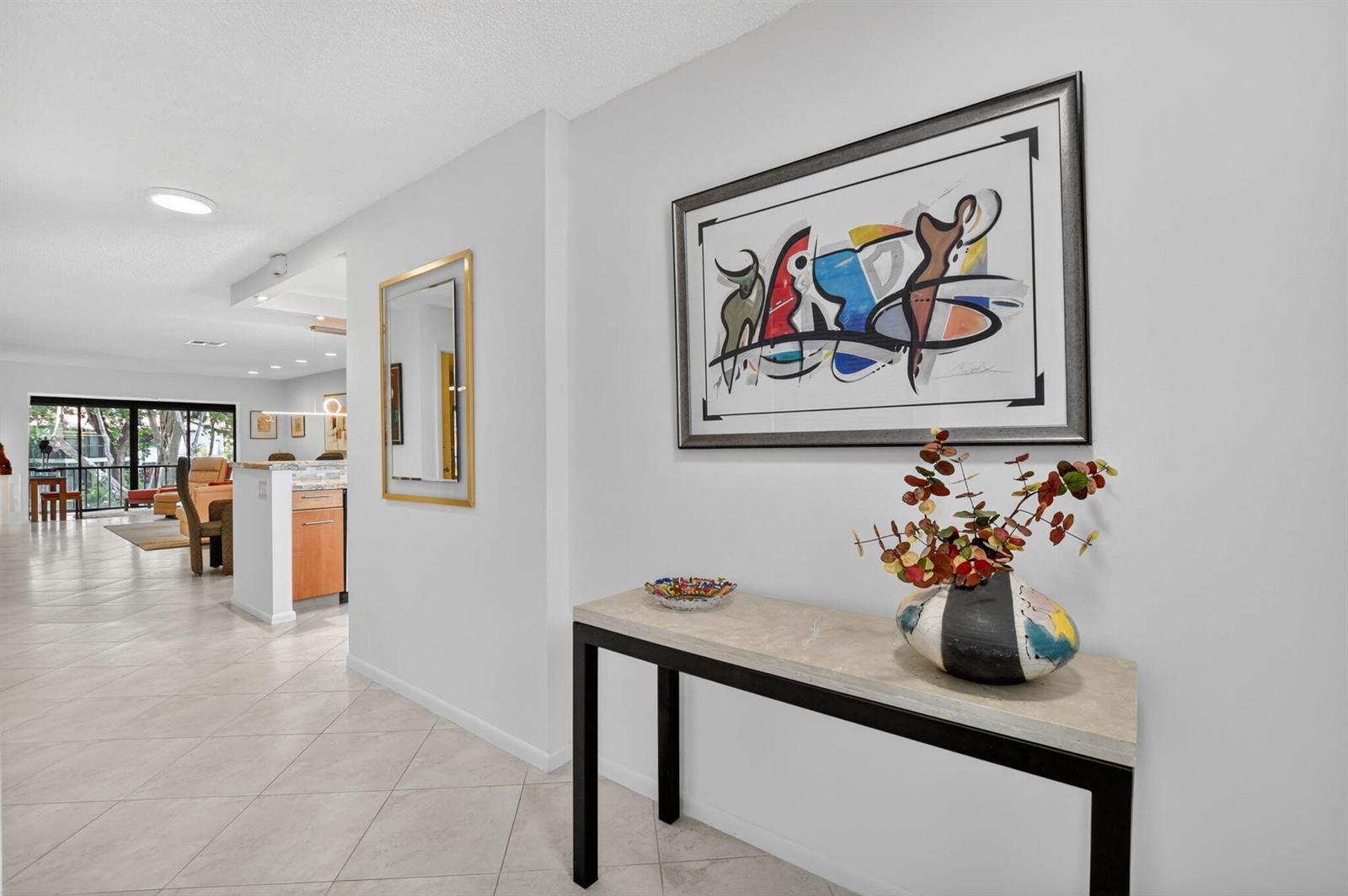 A hallway features a console table with a vase, abstract wall art, and tiled flooring — 8310 Casa Del Lago # D, Boca Raton FL 33433, BOCA RATON, FL