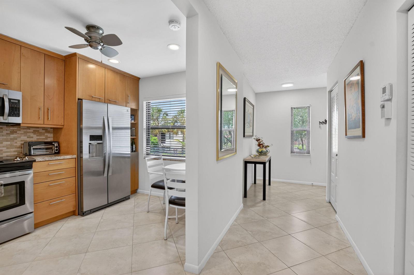 A kitchen with wood cabinets and stainless steel appliances opens into a tiled dining area — 8310 Casa Del Lago # D, Boca Raton FL 33433, BOCA RATON, FL