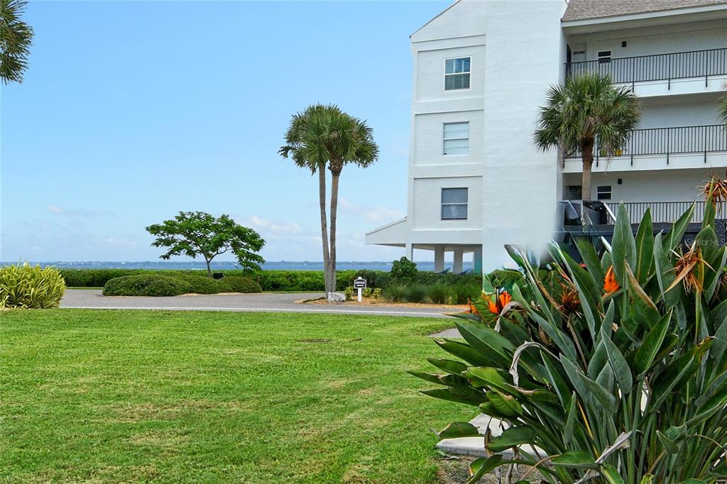 A white multi-story building stands near a grassy lawn, palm trees, and a waterfront view — 4780 GULF OF MEXICO DR. VILLA 5, LONGBOAT KEY, FL