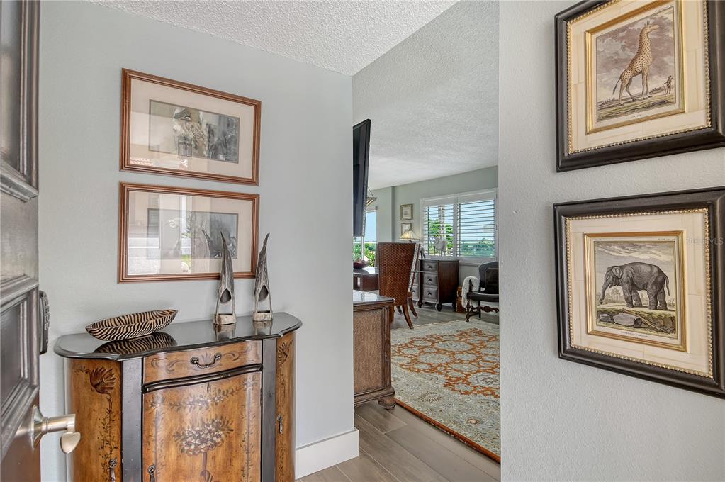 A foyer with a decorative cabinet and framed animal prints leads into a living area — 4780 GULF OF MEXICO DR. VILLA 5, LONGBOAT KEY, FL