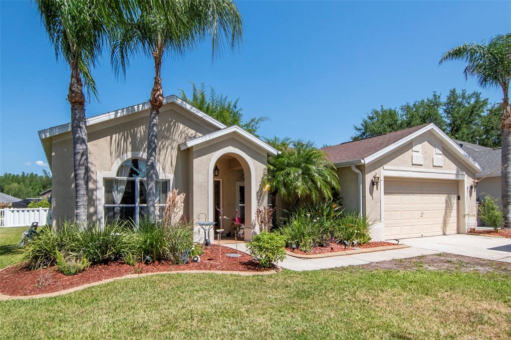 A single-story tan stucco house with a two-car garage and palm trees in the front — 19103 WIND DANCER STREET, LUTZ, FL