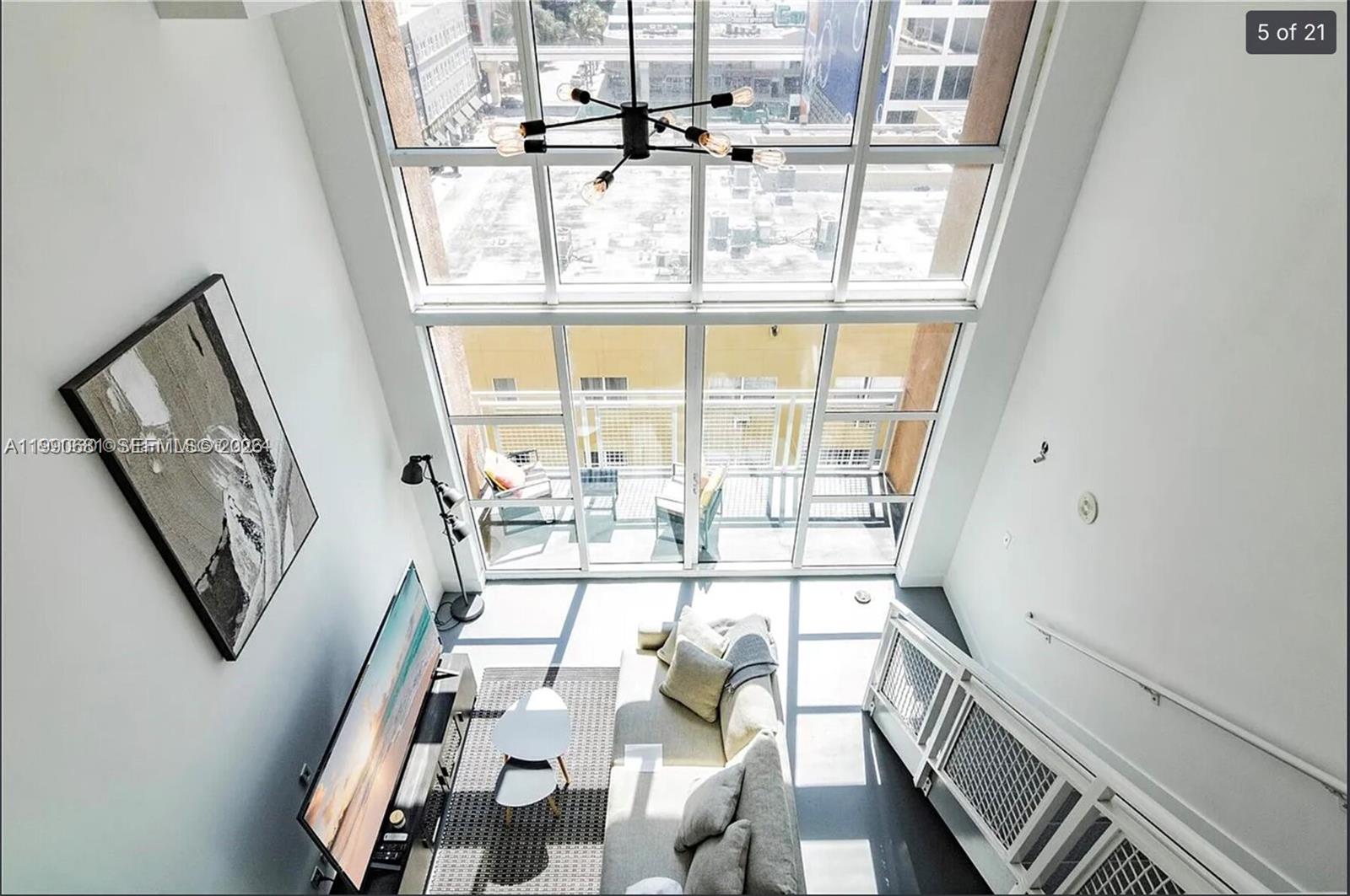 A high-angle view of a modern living room with double-height windows and a balcony — 253 NE 2nd St # 617, Miami FL 33132, MIAMI, FL