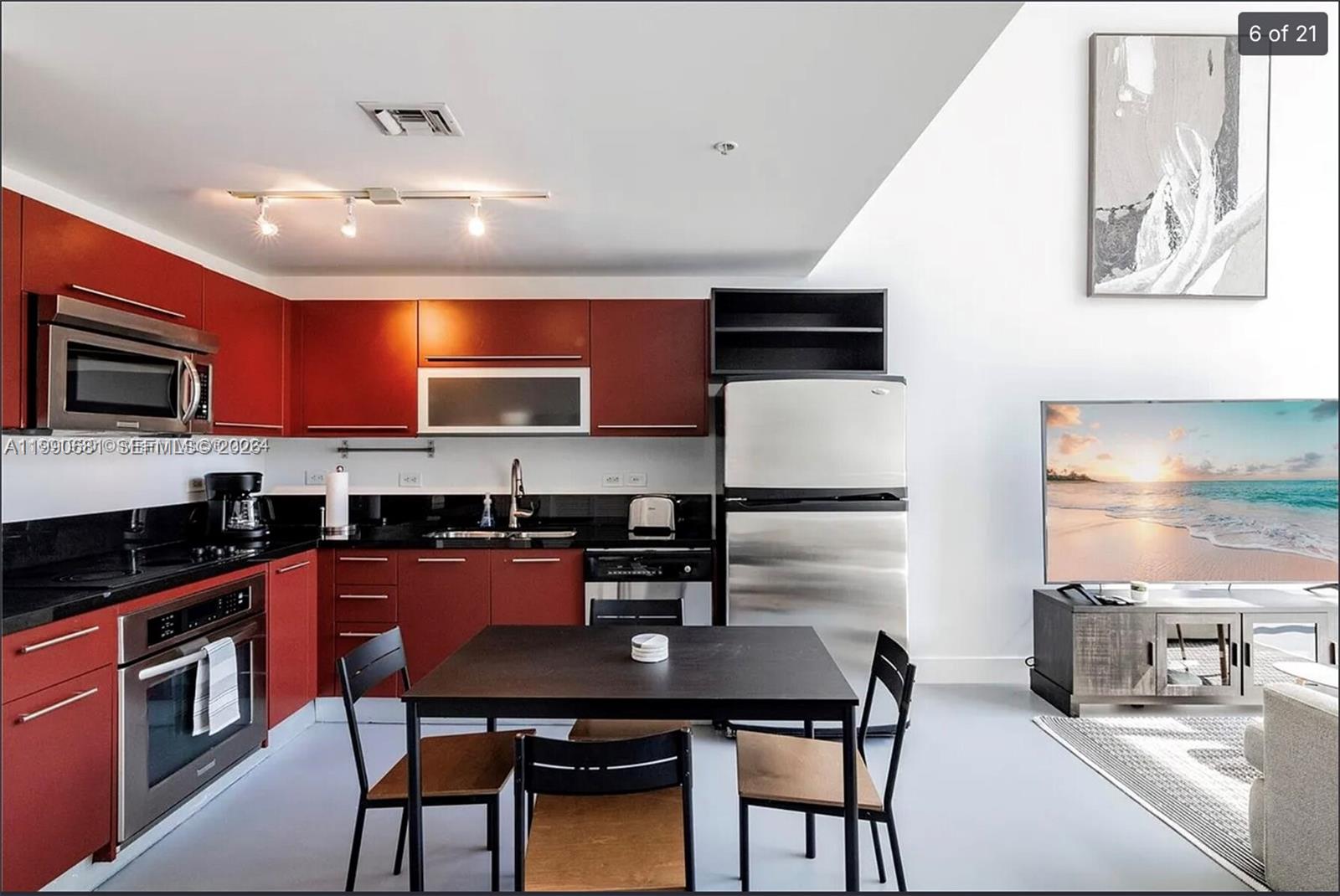 A kitchen with red cabinets, black countertops, and a dining table in an open room — 253 NE 2nd St # 617, Miami FL 33132, MIAMI, FL