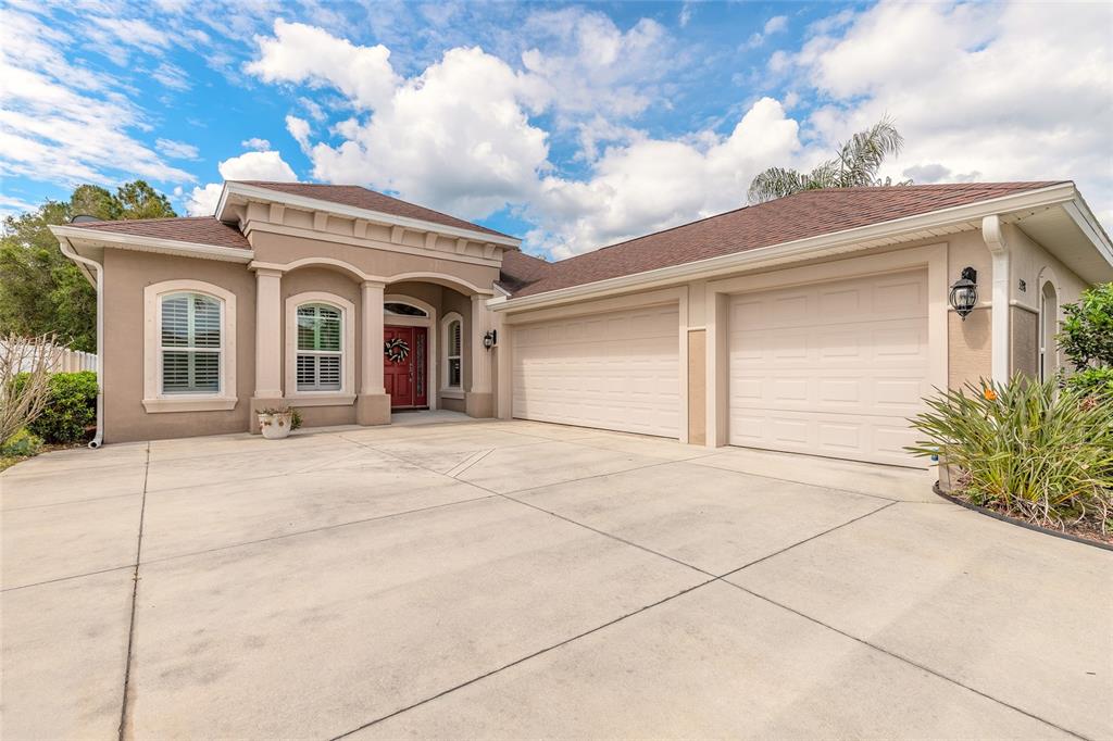 A single-story house with a beige stucco exterior, a red front door, and a two-car garage — 3398 LEONARDO LANE, NEW SMYRNA BEACH, FL