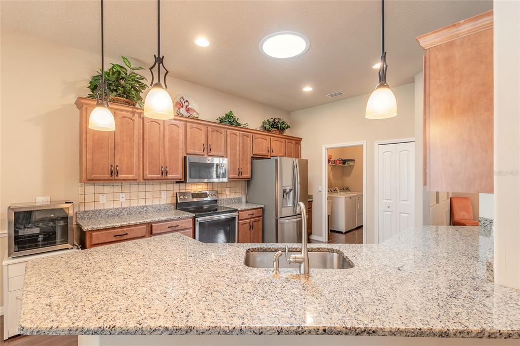A kitchen features wood cabinets, granite countertops, stainless steel appliances, and two pendant lights — 3398 LEONARDO LANE, NEW SMYRNA BEACH, FL