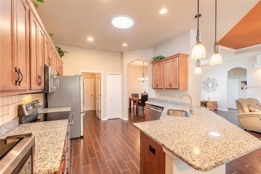 A kitchen with granite countertops, wood cabinets, stainless steel appliances, and dark wood-look tile flooring — 3398 LEONARDO LANE, NEW SMYRNA BEACH, FL