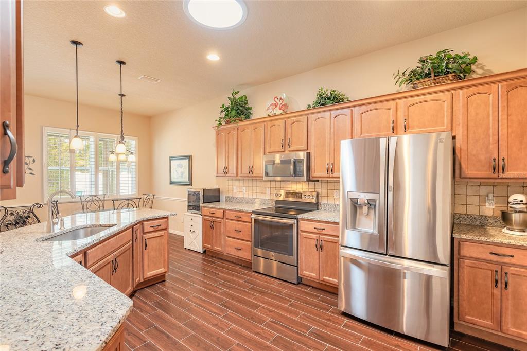 A kitchen with wood cabinets, granite countertops, stainless steel appliances, and wood-look tile flooring — 3398 LEONARDO LANE, NEW SMYRNA BEACH, FL