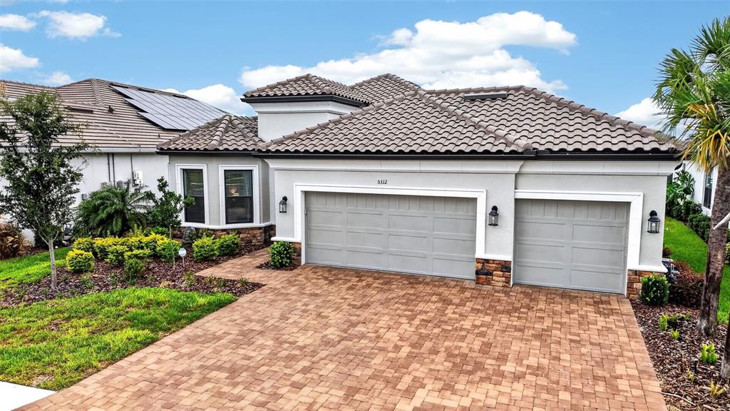 A light-colored house with a tiled roof, three-car garage, and a paved driveway — 5312 CASERTA COURT, PALMETTO, FL