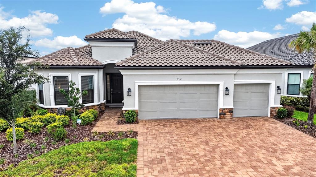 A single-story house with a tiled roof, gray stucco exterior, and a brick paver driveway — 5312 CASERTA COURT, PALMETTO, FL