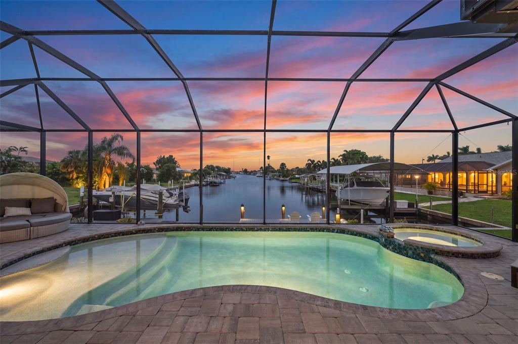 A screened-in pool and spa overlook a canal at sunset with boats docked nearby — 4286 HARBOR BOULEVARD, PORT CHARLOTTE, FL
