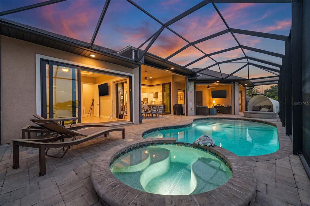 A screened-in patio features a swimming pool, a hot tub, and lounge chairs at sunset — 4286 HARBOR BOULEVARD, PORT CHARLOTTE, FL