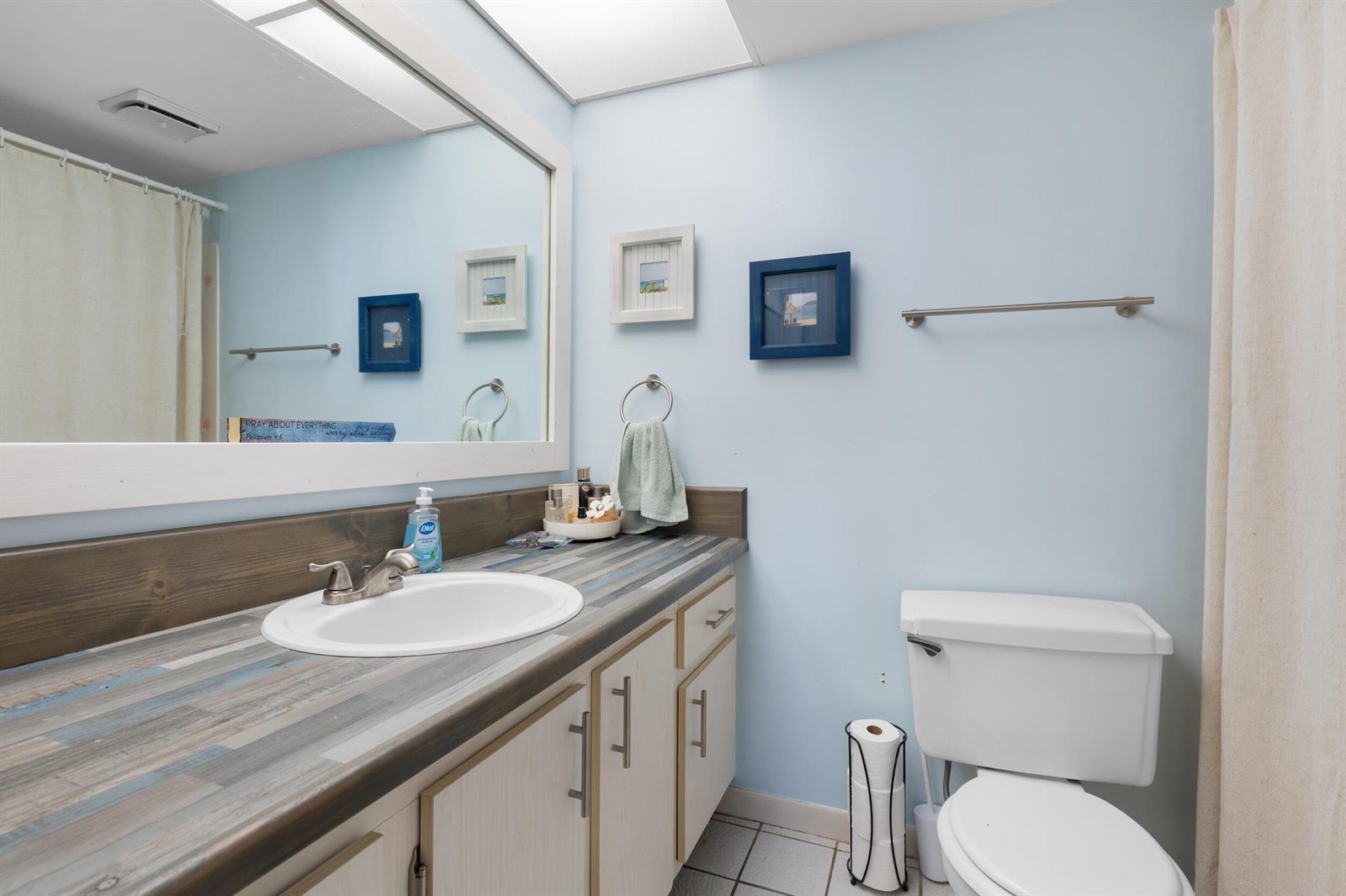 A bathroom features a vanity with a wood-look countertop, a large mirror, and light blue walls — 1270 SE Parkview Place # B5, Stuart FL 34994, STUART, FL