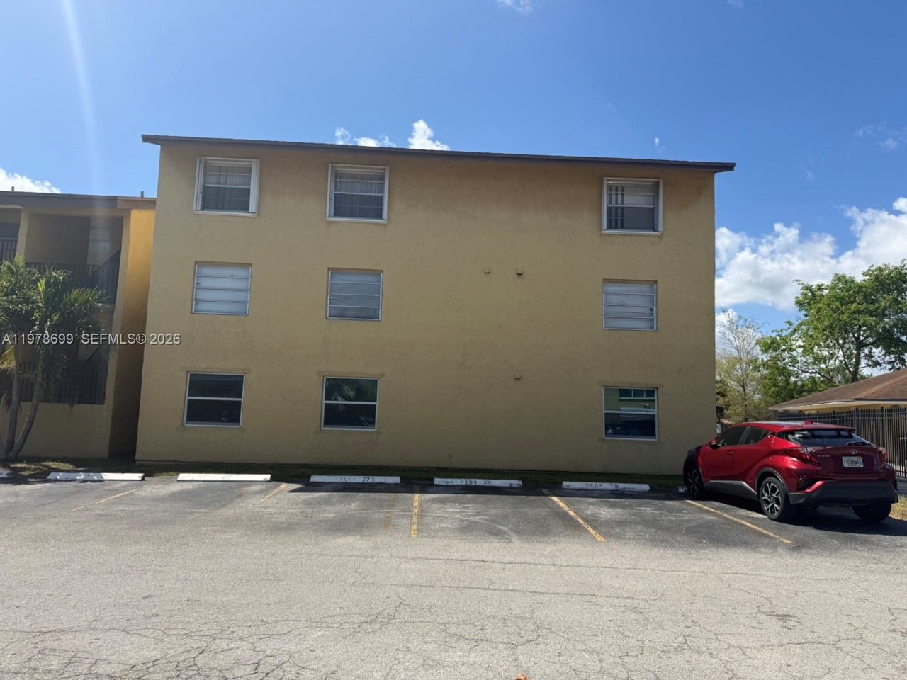 A three-story tan apartment building stands behind a parking lot with a red car — 15470 SW 82nd Ln # 316, Miami FL 33193, MIAMI, FL