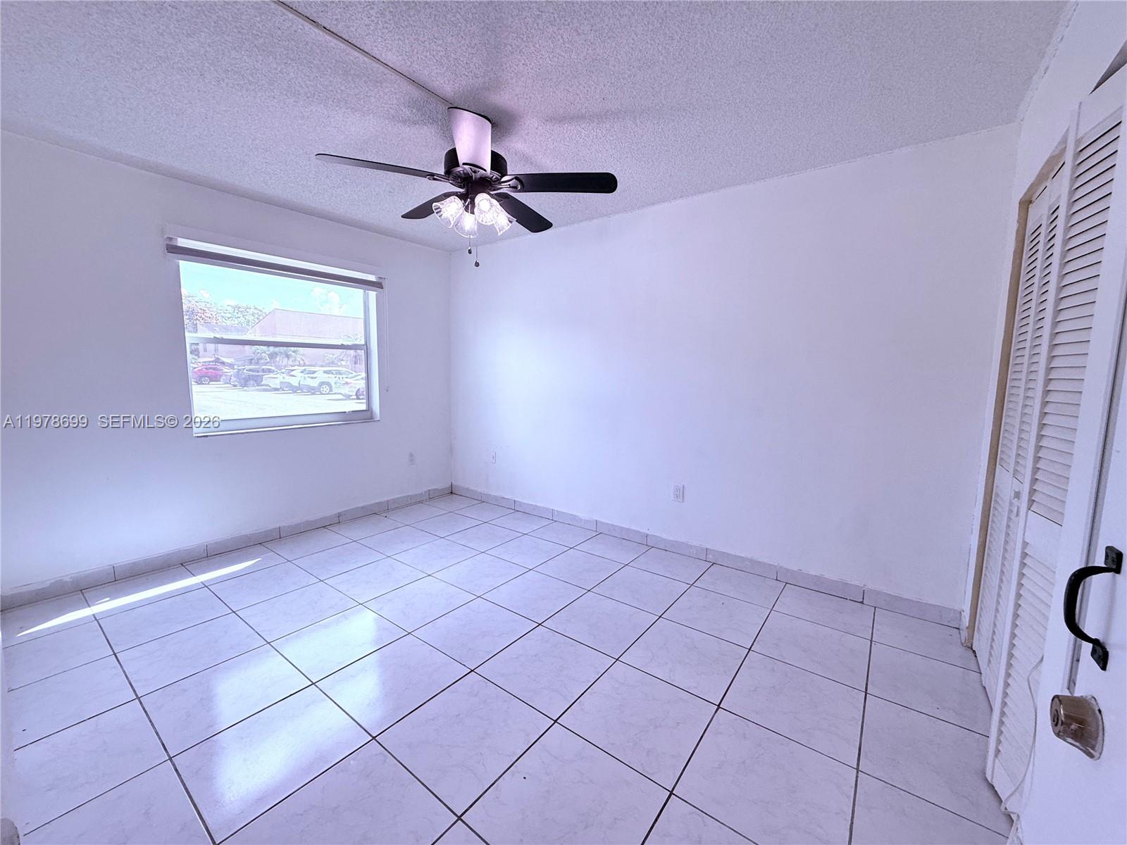 An empty bedroom features white walls, white tile flooring, a ceiling fan, and louvered closet doors — 15470 SW 82nd Ln # 316, Miami FL 33193, MIAMI, FL
