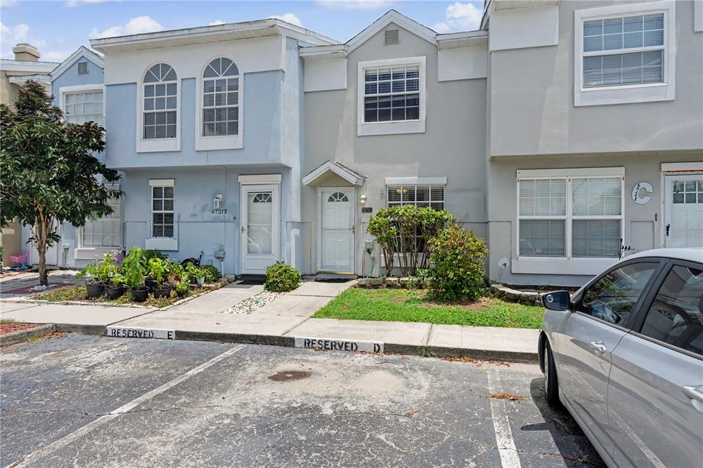 A row of multi-story townhomes features light-colored stucco facades, arched windows, and reserved parking spaces — 6721 121ST AVENUE UNIT D, LARGO, FL