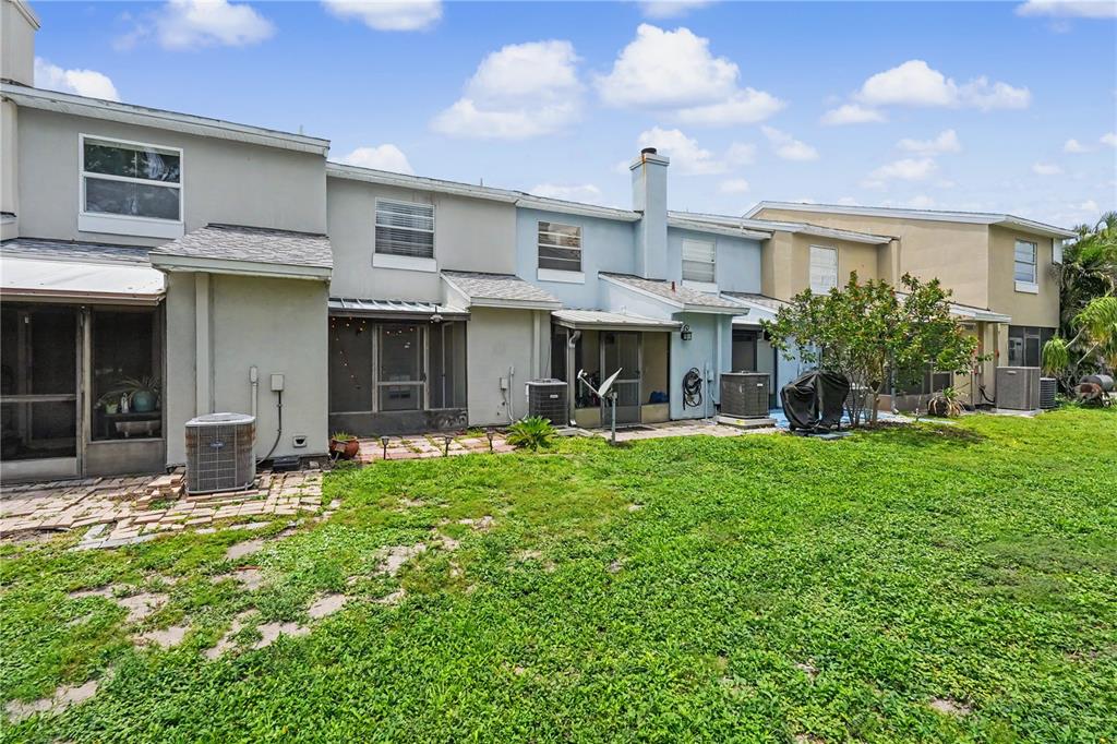 The exterior of a row of multi-story townhomes features screened-in patios and a grassy backyard — 6721 121ST AVENUE UNIT D, LARGO, FL