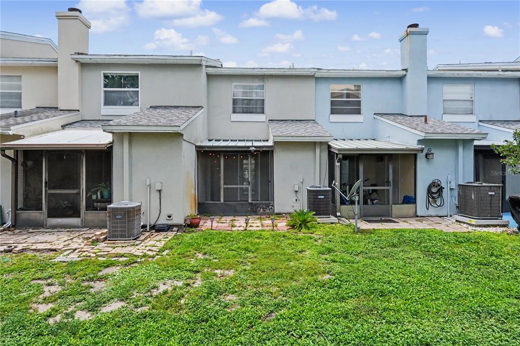 The rear exterior of a multi-unit townhouse features screened-in patios and small concrete paver areas — 6721 121ST AVENUE UNIT D, LARGO, FL