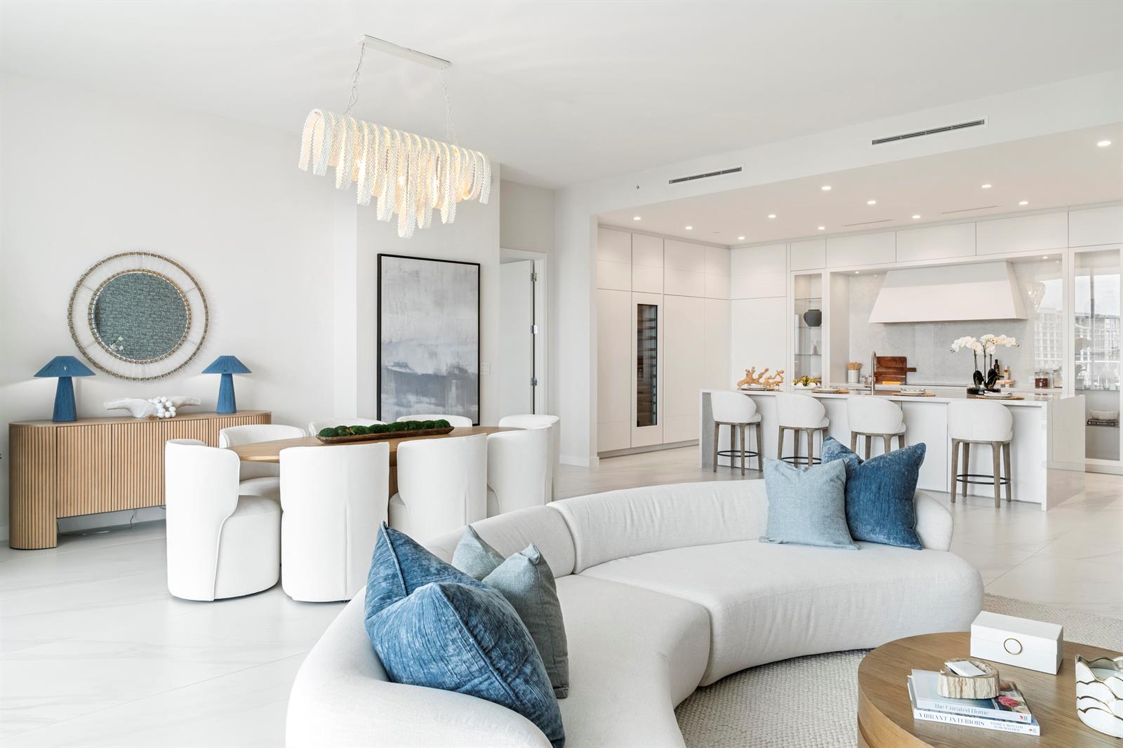A bright, open-concept living and dining area features white furniture, blue accents, and a modern kitchen — 220 SE Mizner Boulevard, Boca Raton FL 33432, BOCA RATON, FL