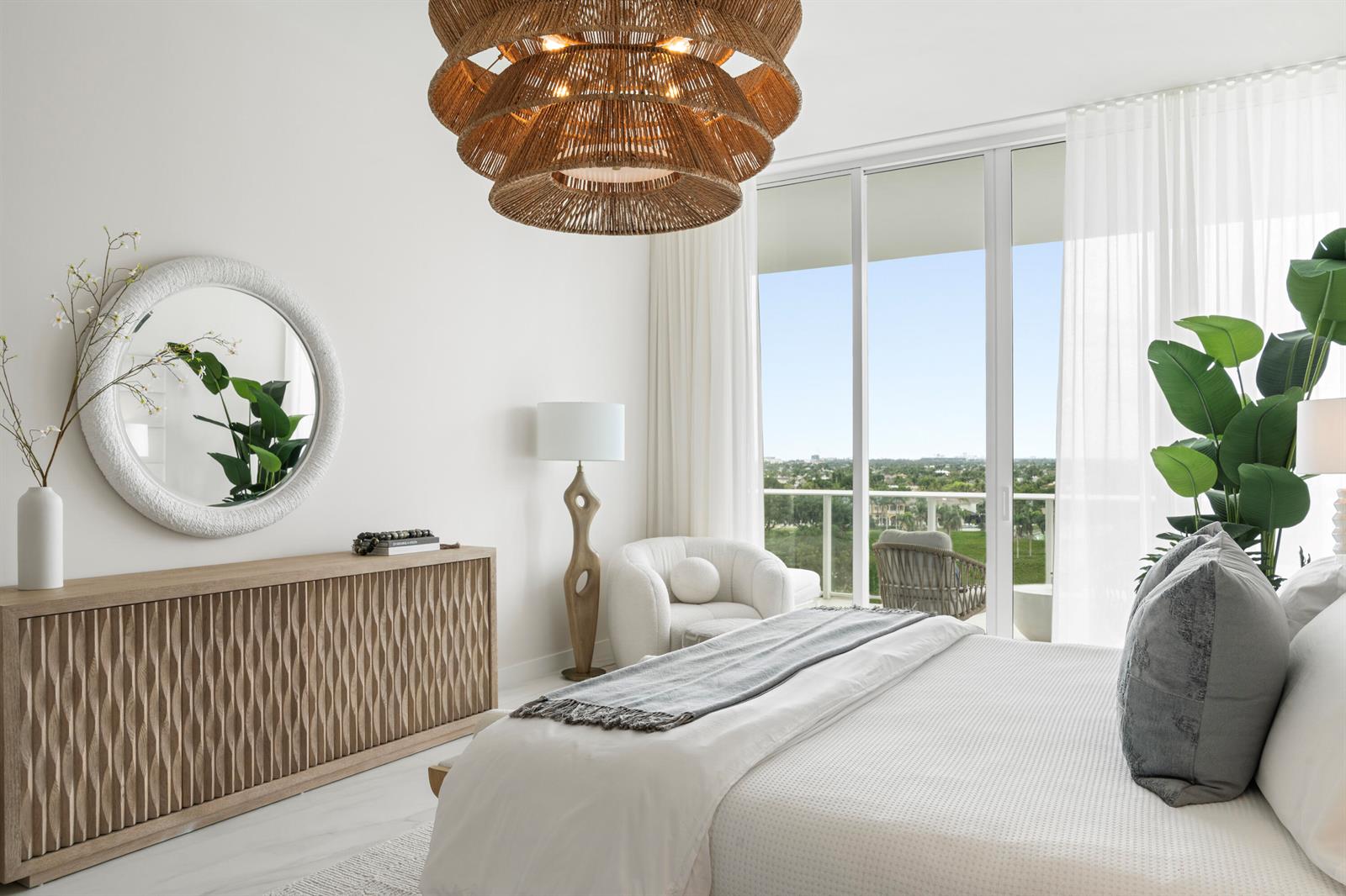 A modern bedroom features a textured wooden dresser, a round mirror, and a large balcony view — 220 SE Mizner Boulevard, Boca Raton FL 33432, BOCA RATON, FL