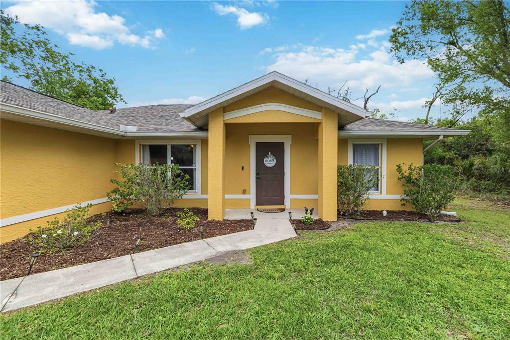 A yellow single-story house features a covered entryway with a brown front door and walkway — 2150 LITTLEFIELD LN, NORTH PORT, FL