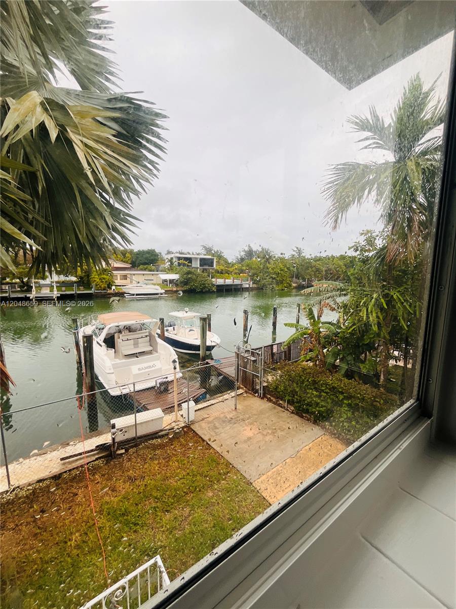 A view through a window shows a canal with two docked boats and lush landscaping — 2045 Calais Dr # 8, Miami Beach FL 33141, MIAMI BEACH, FL
