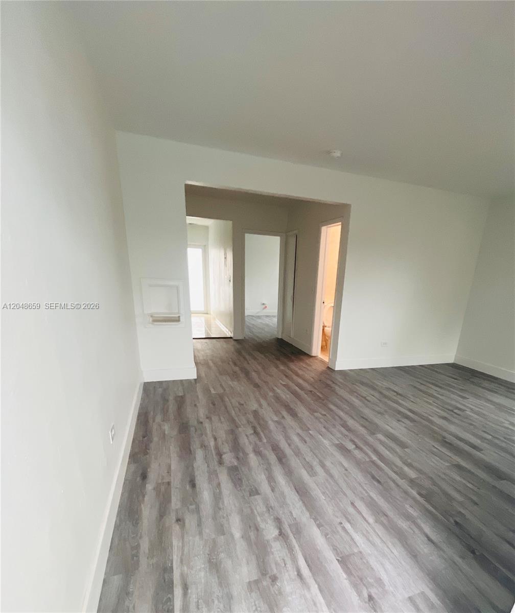An empty room with white walls and gray wood-look flooring leads to a hallway — 2045 Calais Dr # 8, Miami Beach FL 33141, MIAMI BEACH, FL