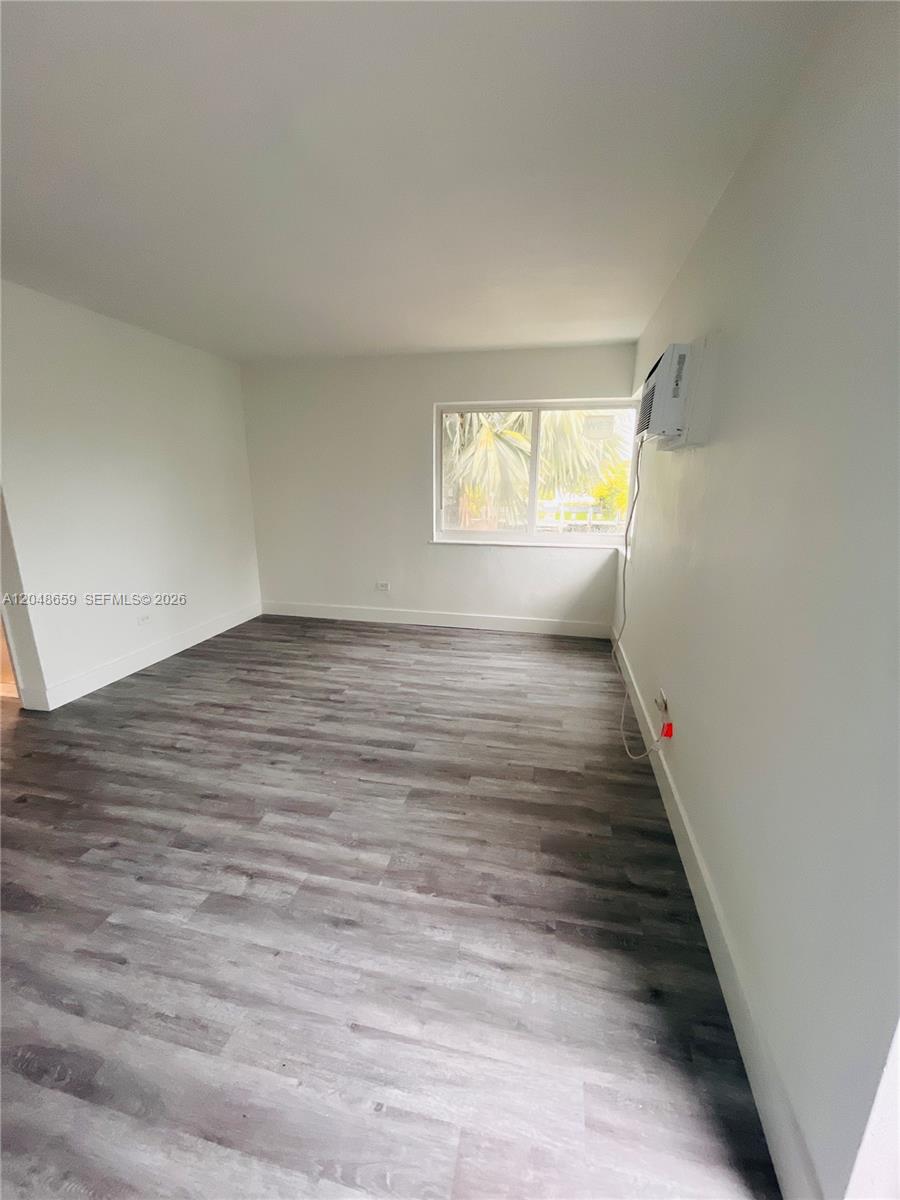 An empty room features light gray walls, wood-look flooring, and a window air conditioning unit — 2045 Calais Dr # 8, Miami Beach FL 33141, MIAMI BEACH, FL