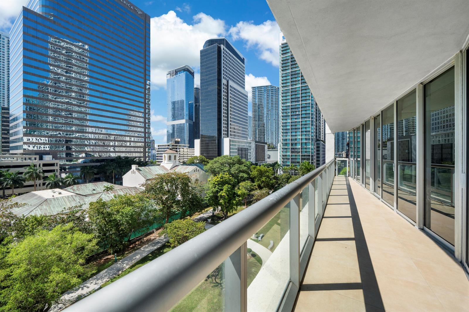 A balcony with a glass railing overlooks a park and surrounding city skyscrapers — 495 Brickell Avenue # 811, Miami FL 33131, MIAMI, FL