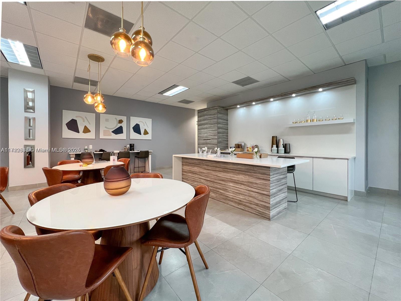 A modern office breakroom features two round tables, a kitchen island, and contemporary pendant lighting — 1200 Brickell Bay Dr # 2007, Miami FL 33131, MIAMI, FL