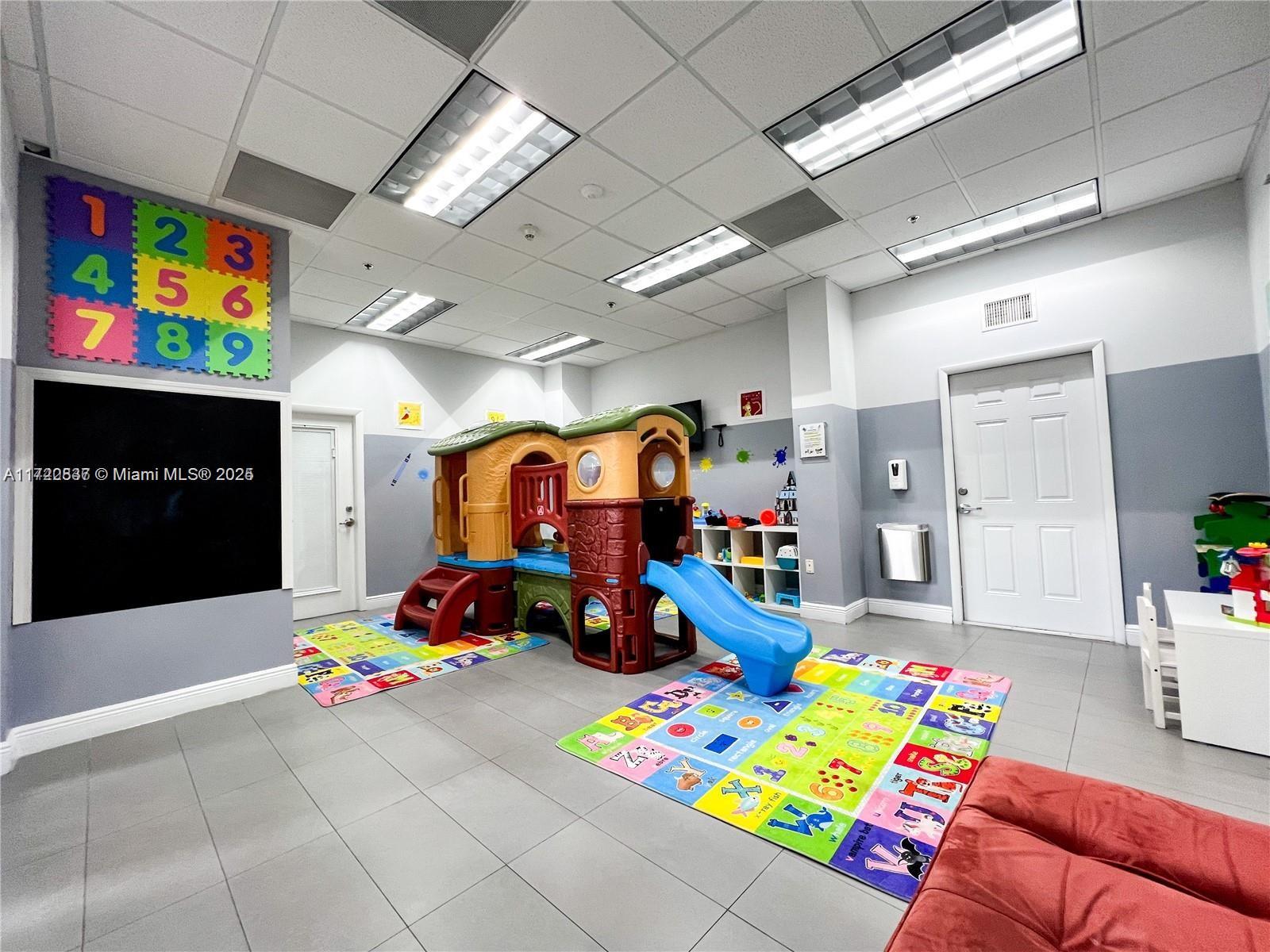 A brightly lit indoor playroom features a plastic jungle gym, colorful floor mats, and tile flooring — 1200 Brickell Bay Dr # 2007, Miami FL 33131, MIAMI, FL
