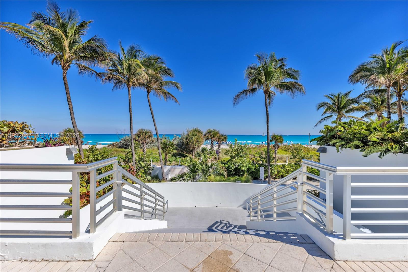 A concrete staircase with metal railings leads down toward a beach with palm trees — 5161 Collins Ave # 410, Miami Beach FL 33140, MIAMI BEACH, FL