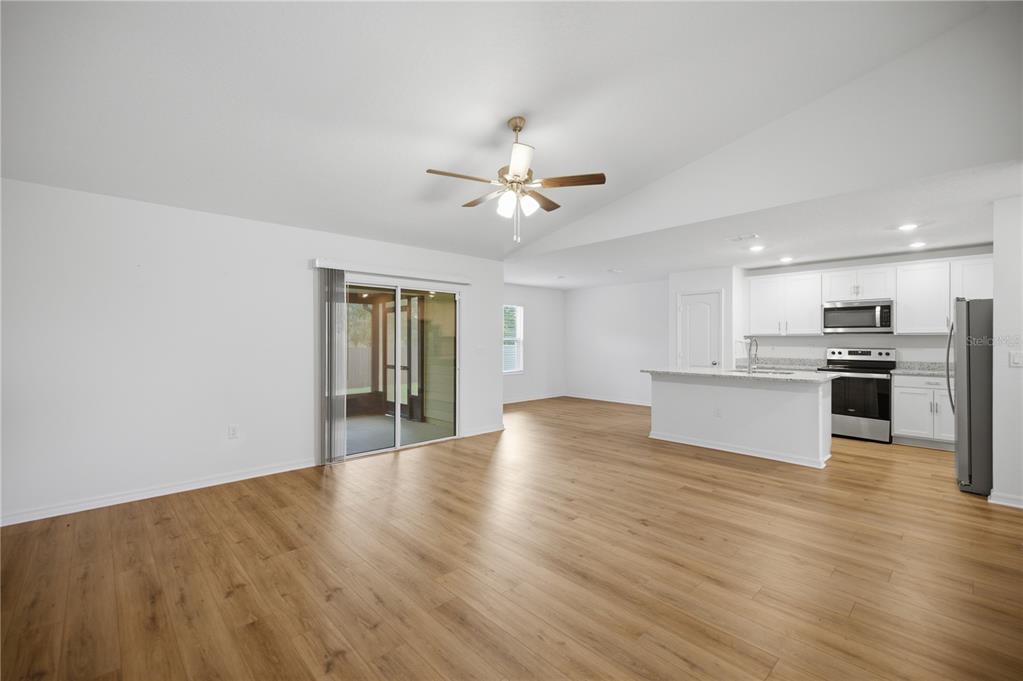 An open-concept living area features light wood-look flooring, white walls, and an adjacent kitchen — 3125 SW 172ND LANE ROAD, OCALA, FL