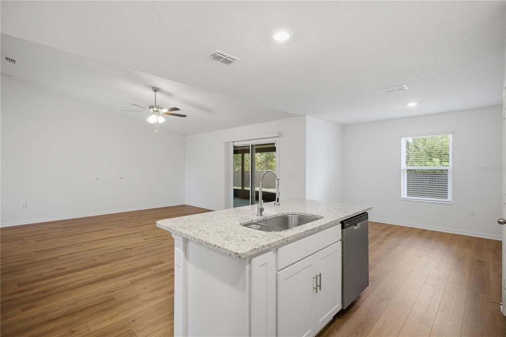 A kitchen island with a sink and dishwasher overlooks an open-concept living area with wood-look flooring — 3125 SW 172ND LANE ROAD, OCALA, FL