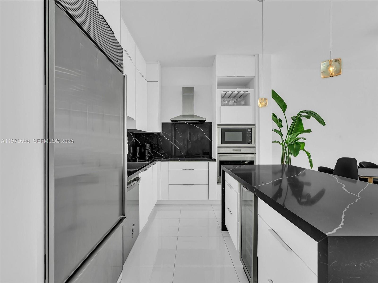 A modern kitchen features white cabinetry, black marble countertops, stainless steel appliances, and tile flooring — 2020 N Bayshore Dr # 3303, Miami FL 33137, MIAMI, FL