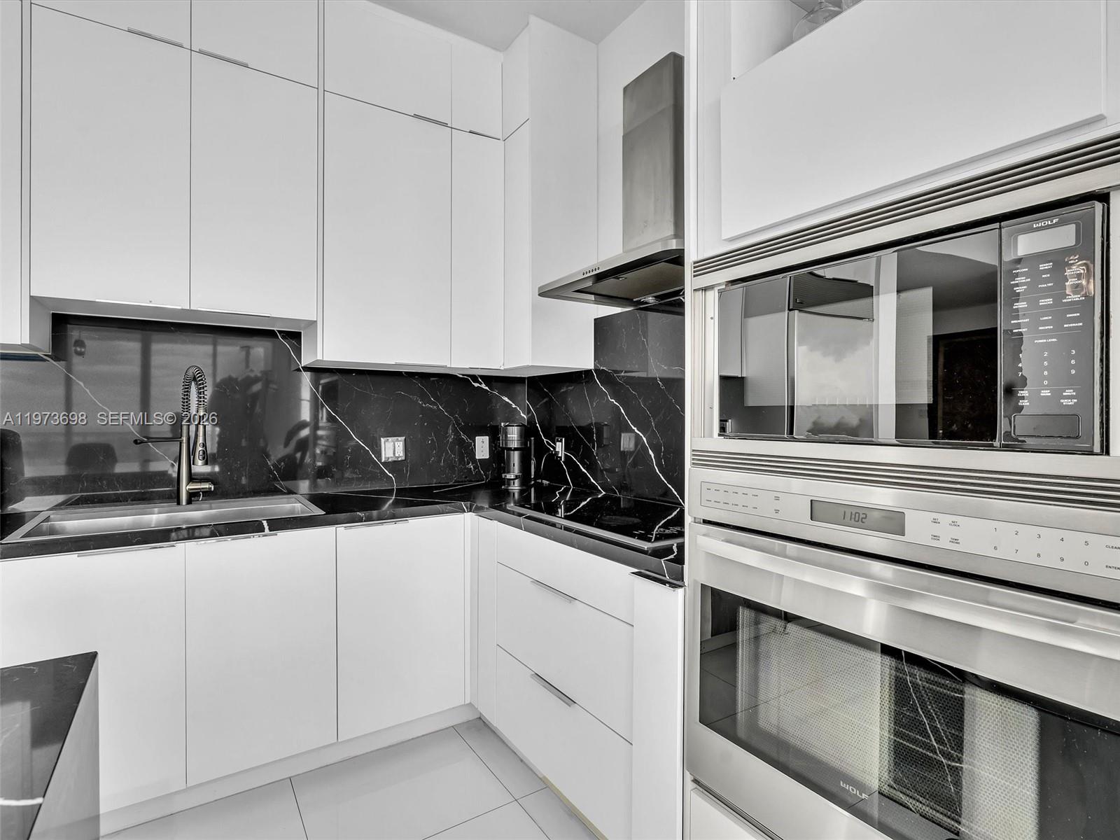 A modern kitchen features white cabinets, black marble countertops, and stainless steel Wolf appliances — 2020 N Bayshore Dr # 3303, Miami FL 33137, MIAMI, FL