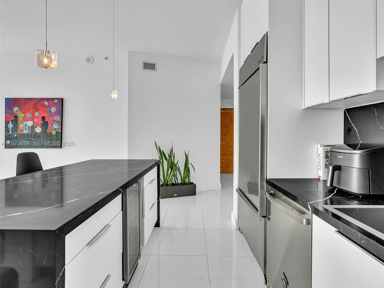 A modern kitchen features white cabinetry, black marble countertops, stainless steel appliances, and tile flooring — 2020 N Bayshore Dr # 3303, Miami FL 33137, MIAMI, FL