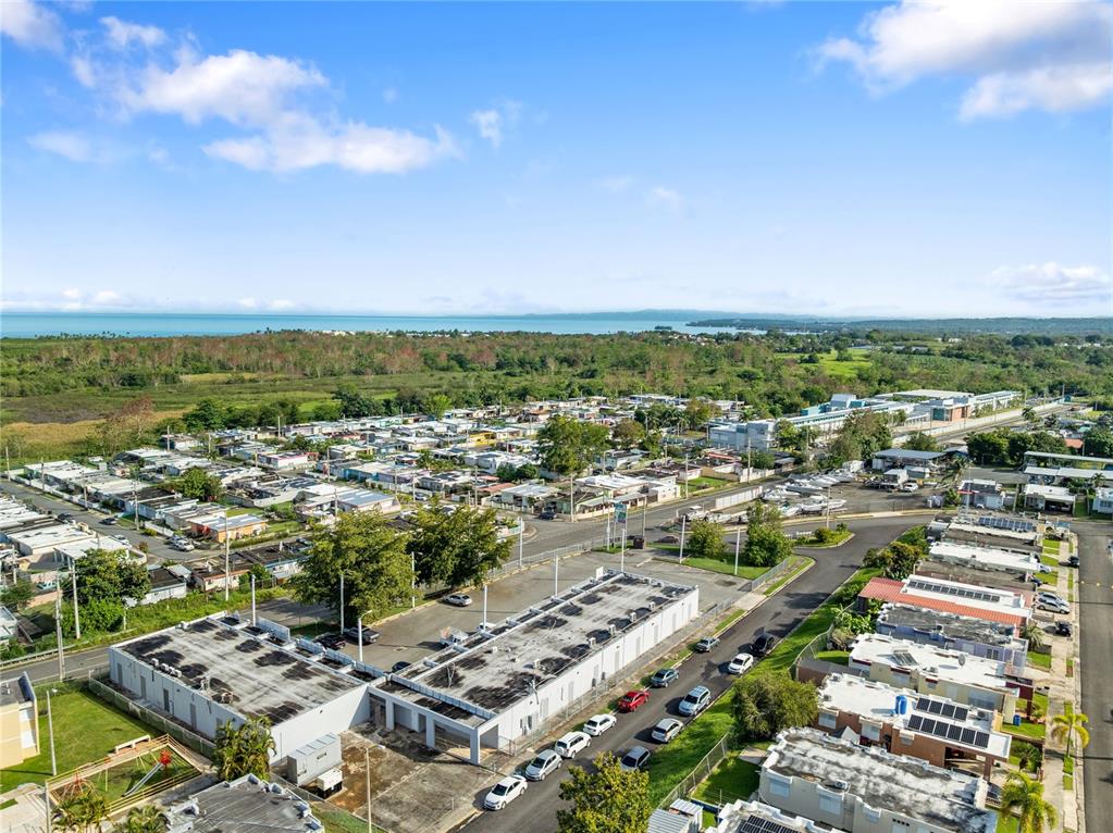 An aerial view shows a residential neighborhood with flat-roofed buildings, paved streets, and distant water — 308 KM 5.3, CABO ROJO, PR