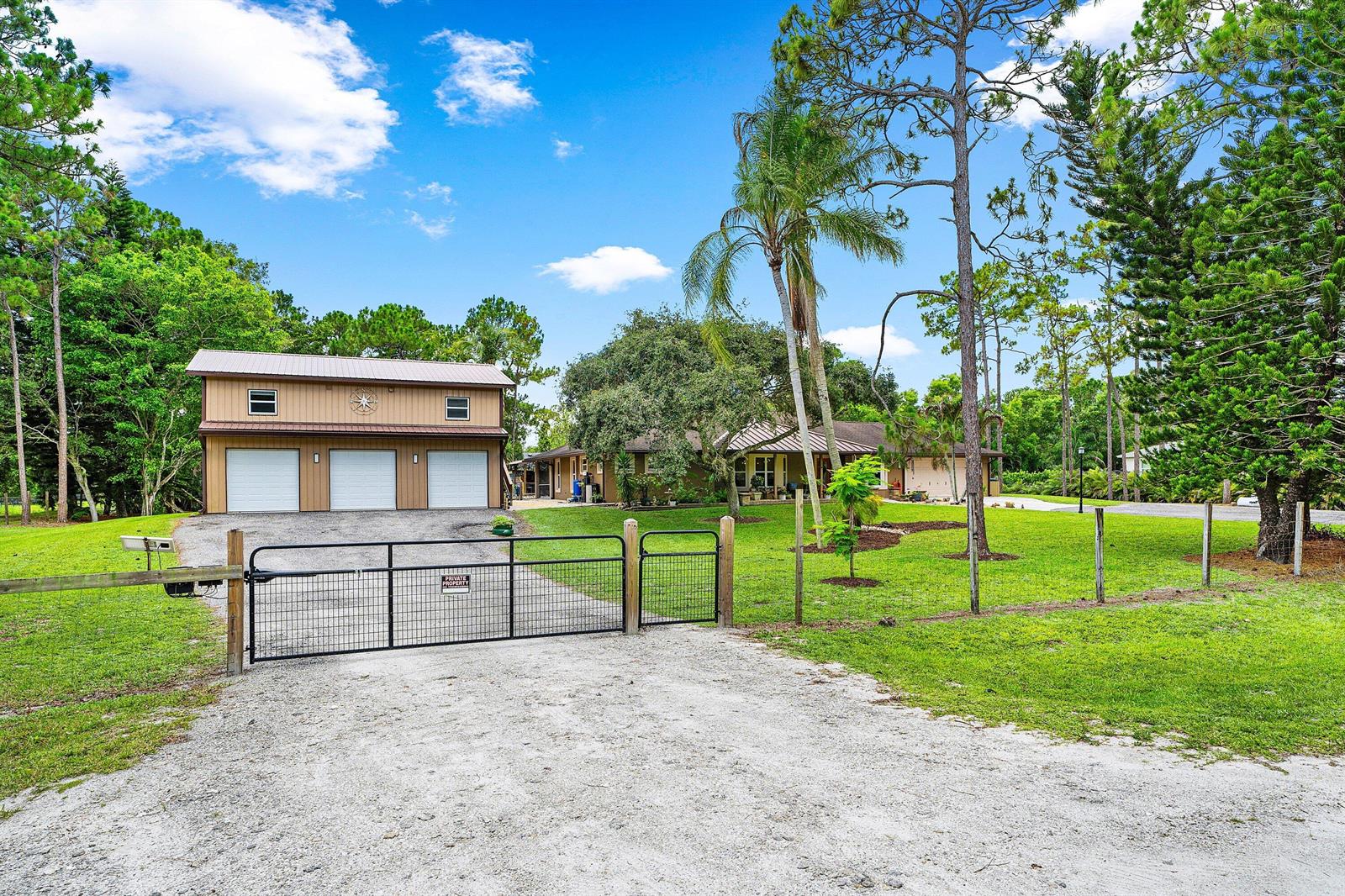 A detached three-car garage and a single-story house sit behind a metal gate on grass — 14732 63rd Court N, Loxahatchee FL 33470, LOXAHATCHEE, FL