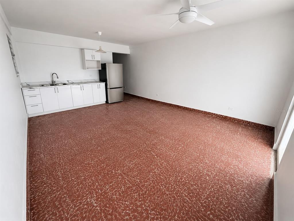 An open-concept room features white kitchen cabinets, a stainless steel refrigerator, and reddish-brown tile flooring — 2844 ROOSEVELT UNIT 302, PONCE, PR