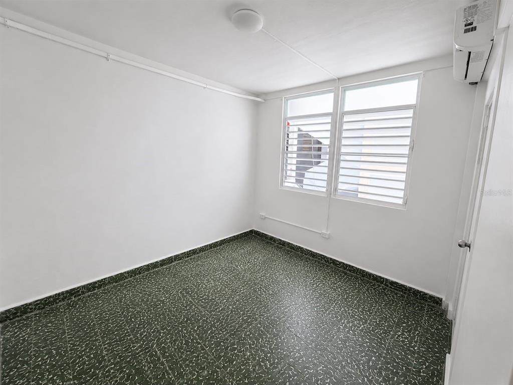 An empty room features white walls, a green speckled tile floor, and louvered windows — 2844 ROOSEVELT UNIT 302, PONCE, PR