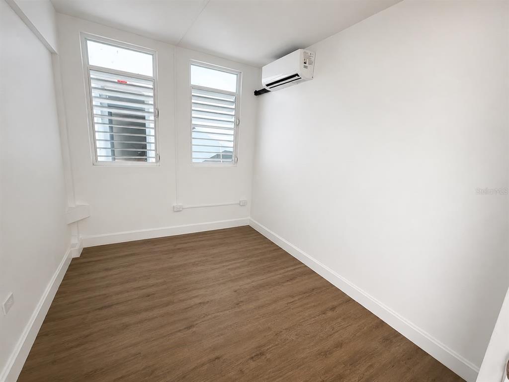 An empty room with white walls, wood-look flooring, two louvered windows, and a wall-mounted air conditioner — 2844 ROOSEVELT UNIT 302, PONCE, PR