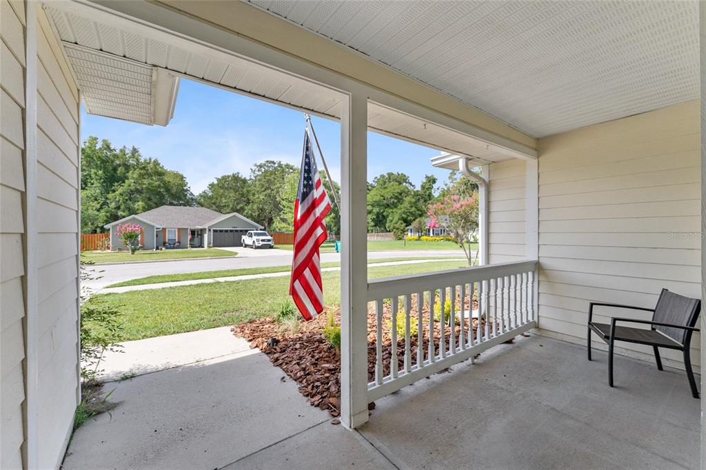 A covered front porch features a concrete floor, white railings, and an American flag — 25670 NW 9TH ROAD, NEWBERRY, FL