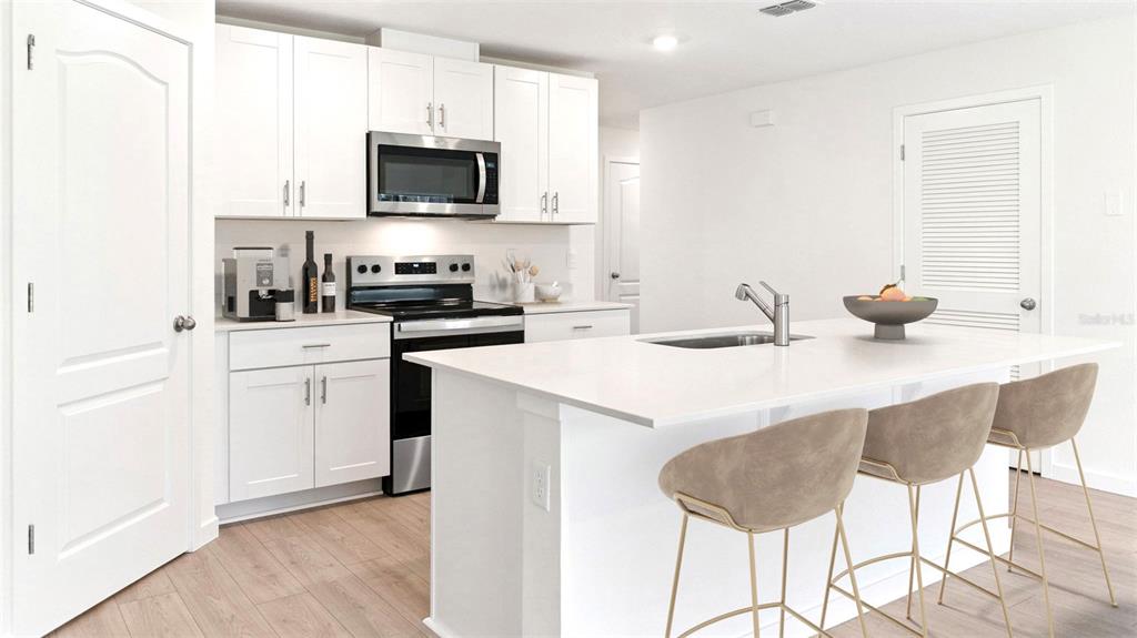 A modern kitchen features white cabinetry, stainless steel appliances, and a central island with seating — 1476 MORNING WALK DRIVE, ORMOND BEACH, FL
