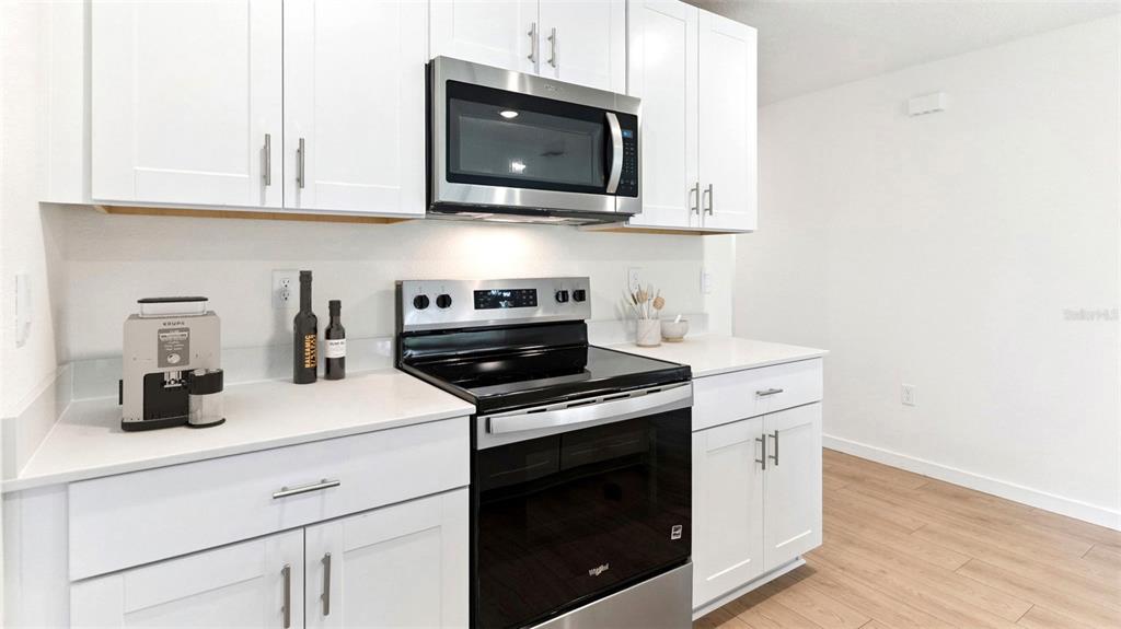 A kitchen features white cabinets, stainless steel appliances, and light wood-look flooring — 1476 MORNING WALK DRIVE, ORMOND BEACH, FL