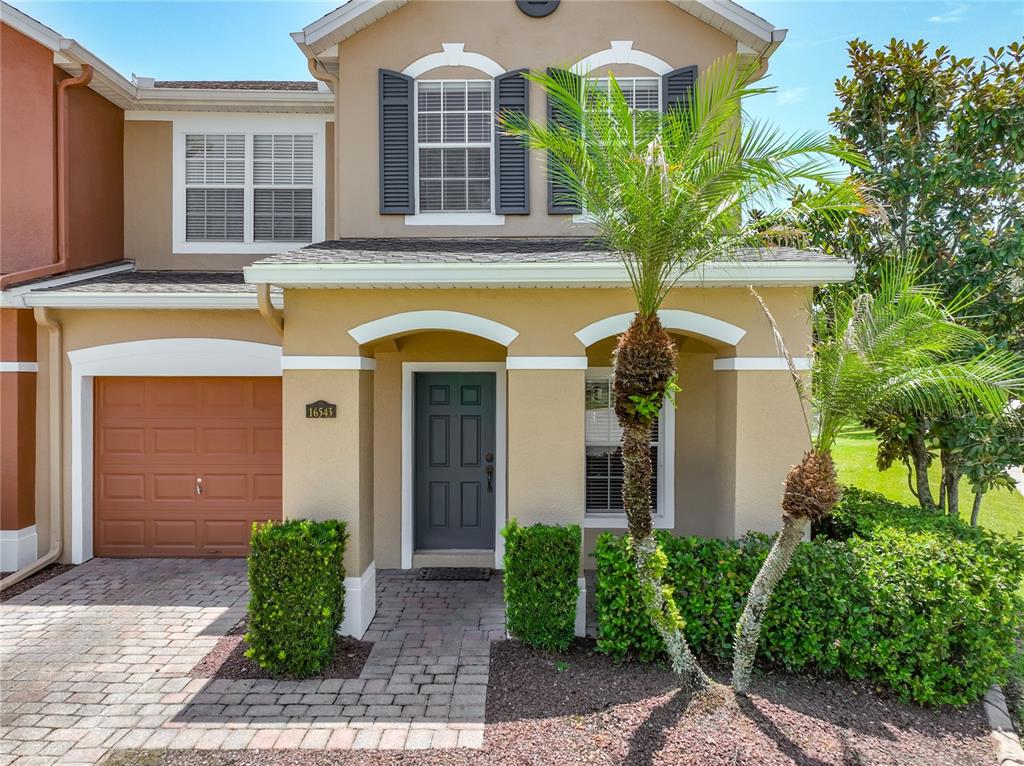 A two-story tan townhouse features a brown garage door, a dark front door, and landscaping — 16543 CEDAR CREST DRIVE, ORLANDO, FL