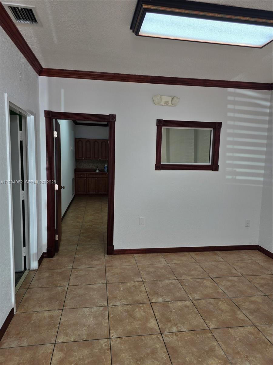A room with tan tile flooring, white walls, dark wood trim, and a rectangular wall mirror — 1745 W 37th St # 17, Hialeah FL 33012, HIALEAH, FL